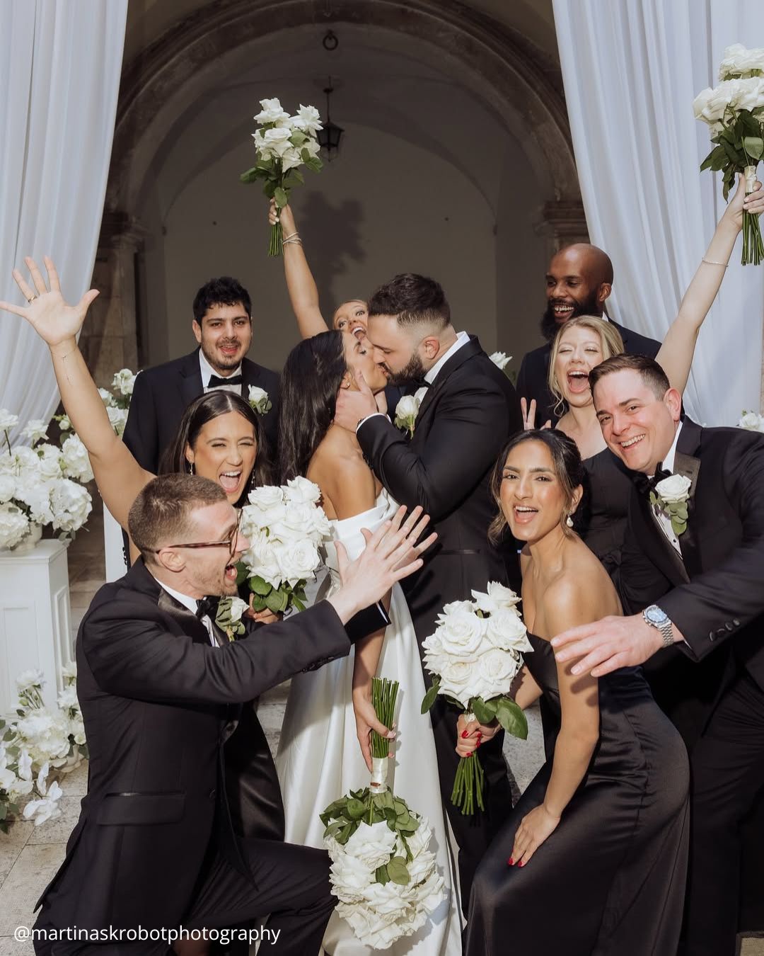 wedding photos brides kissing with fun friends all with a bouquet in hands in black and white colors martinaskrobotphotography